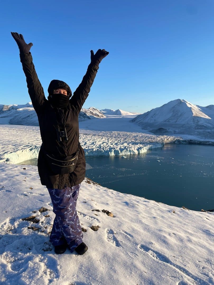 a woman standing on a snowy mountain with her arms up in the air